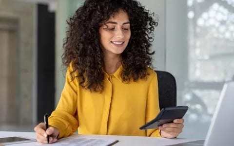 Professional woman with curly hair holding phone writing notes